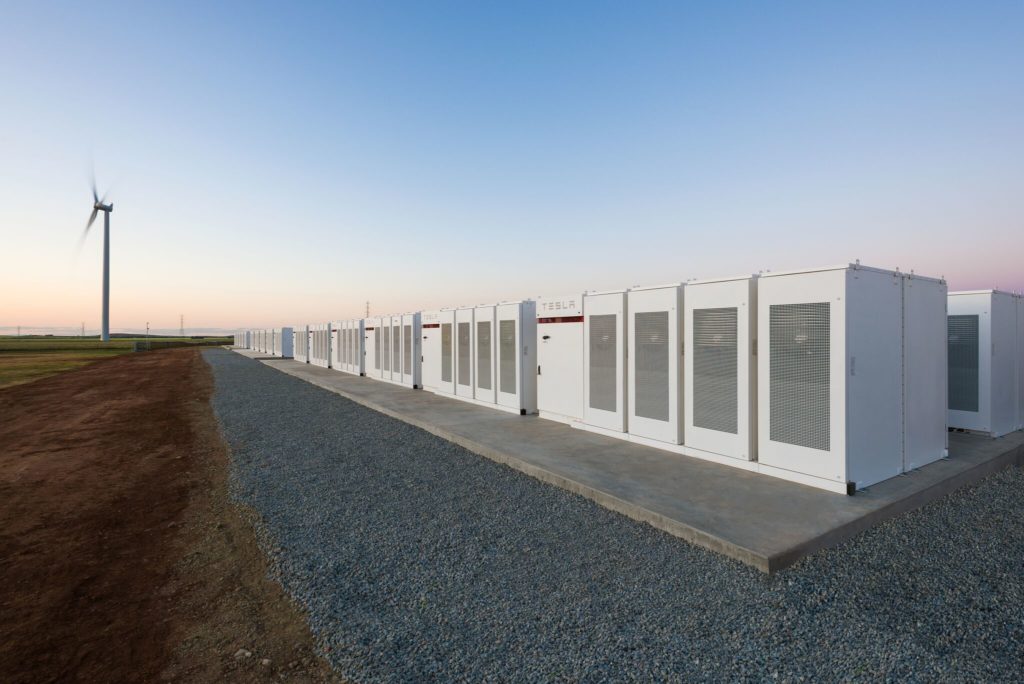 Tesla big battery in Hornsdale, South Australia, with a wind turbine spinning in the background