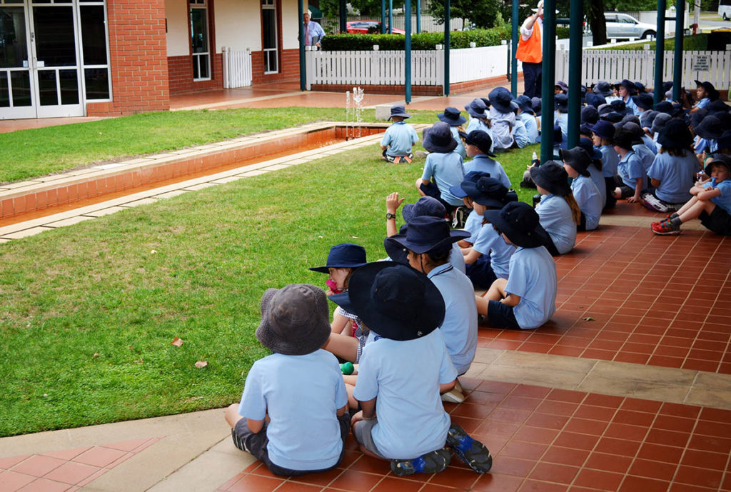 Schoolkids sit in the shade in summer uniform