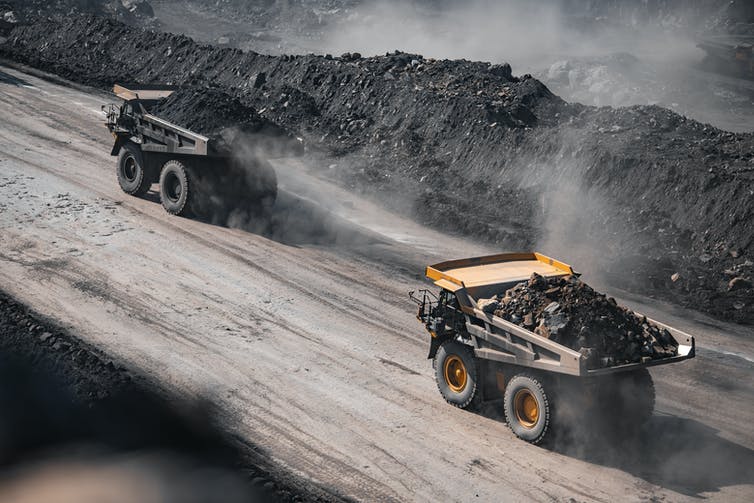 A line of heavy machinery delivering tray-fulls of coal from a mine.