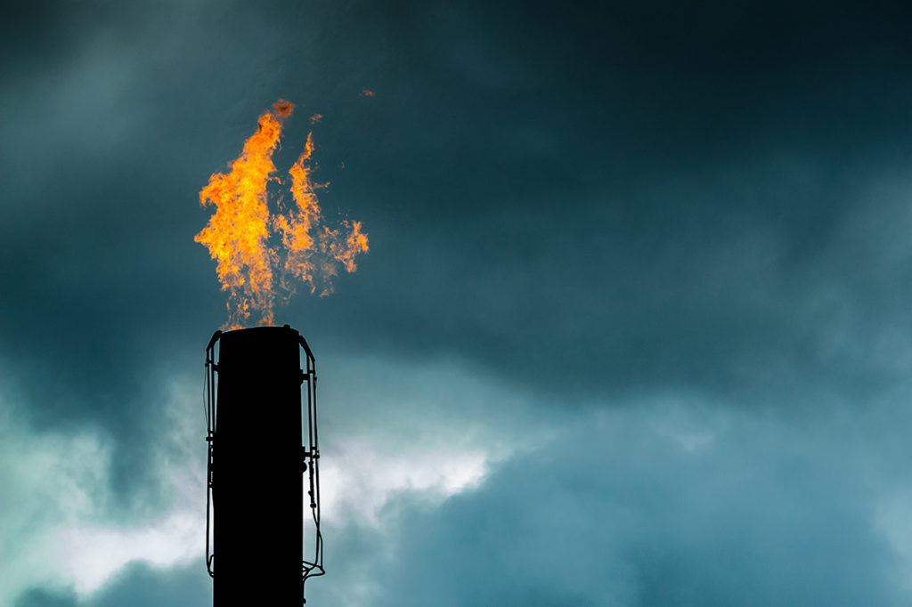 A silhouetted stack flaring gas against a stormy sky.