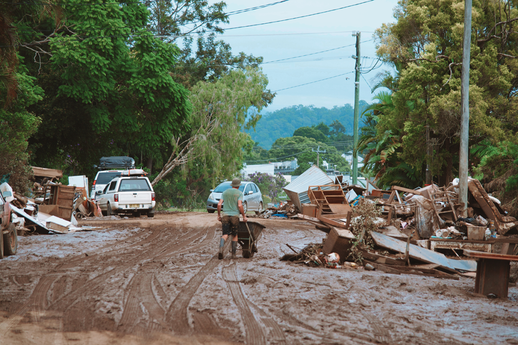 An image of a man cleaning up the mud in a flood affected town with a wheelbarrow.