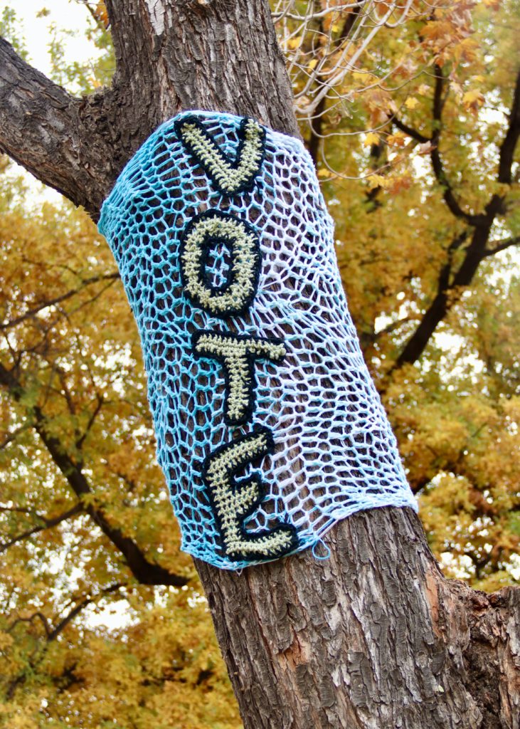 A knitted VOTE sign wraps around a tree