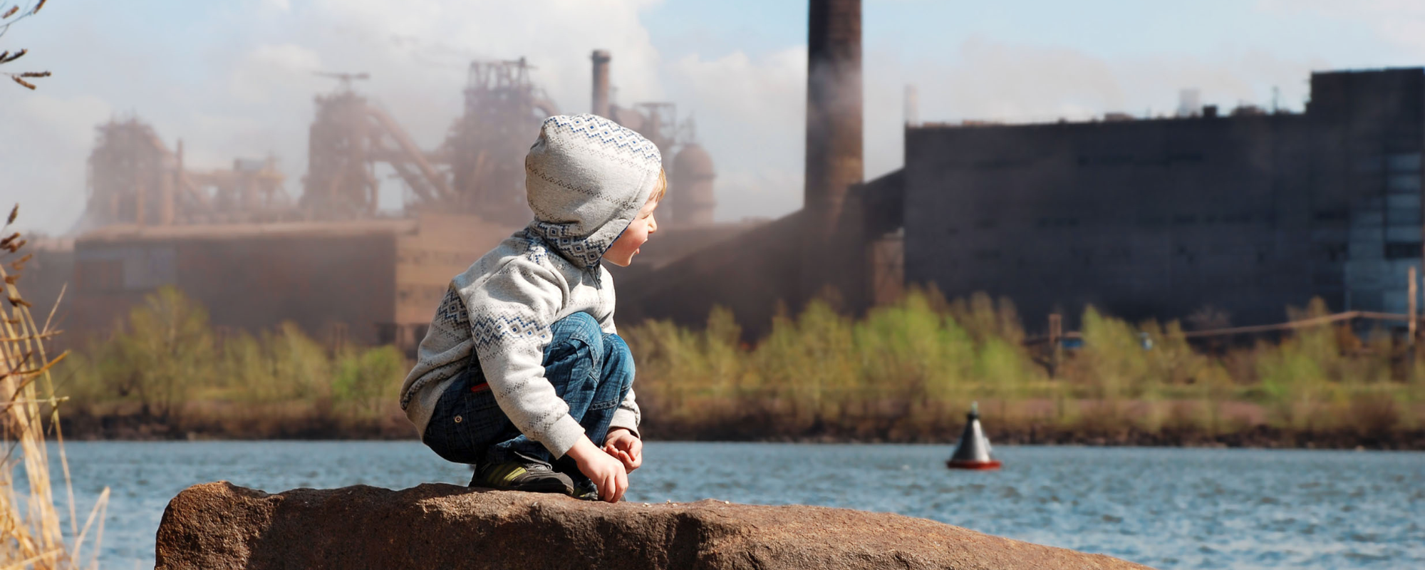 Child sitting on a rock in front of industrial area